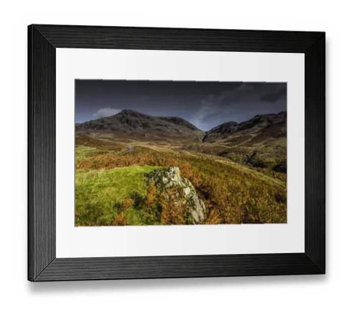Framed Print : View of road snaking towards upland pass, with volcanic rock in foreground, Hardknott Pass, Lake District N. P