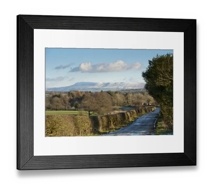 Framed Print : View of icy rural road, hedgerow and bare trees towards snow covered hill in distance, looking from Little Bowland Road toward Pendle Hill, Chipping, Lancashire, England, december