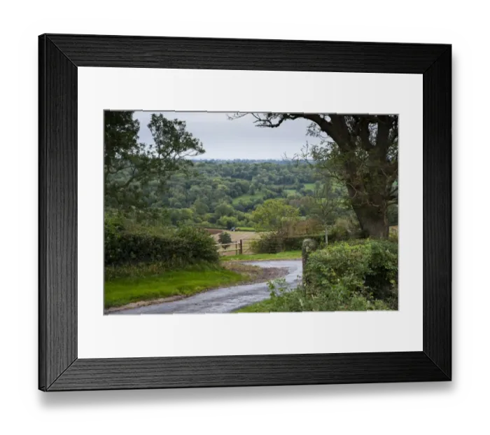 Framed Print : View of farm track, tractor ploughing in field and woodland on slope in distance, Shepton Mallet, Somerset, England Framed Print : View of farm track, tractor ploughing in field and woodland on slope in distance, Shepton Mallet, Somerset, England