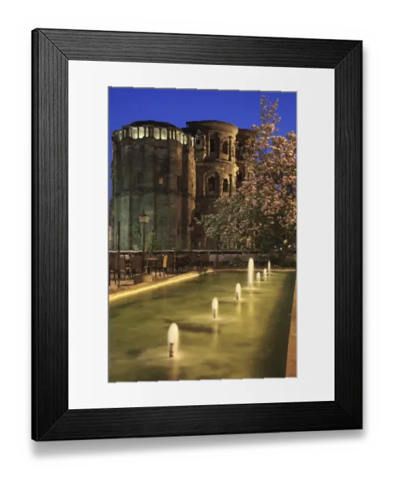 Framed Print : Roman city gate with fountains and flowering magnolia in foreground, illuminated at night, Porta Nigra, Trier