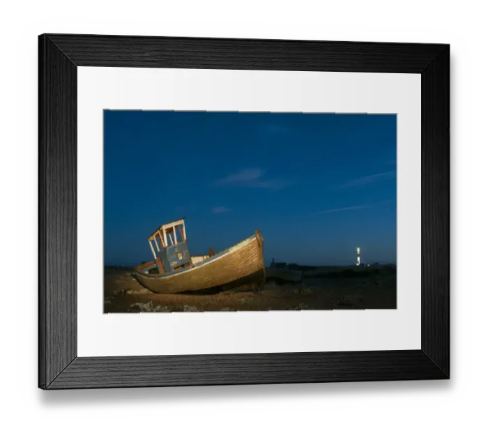 Framed Print : Abandoned fishing boat on shingle beach illuminated by torchlight at night, with distant lighthouse, Dungeness, Kent Framed Print : Abandoned fishing boat on shingle beach illuminated by torchlight at night, with distant lighthouse, Dungeness, Kent