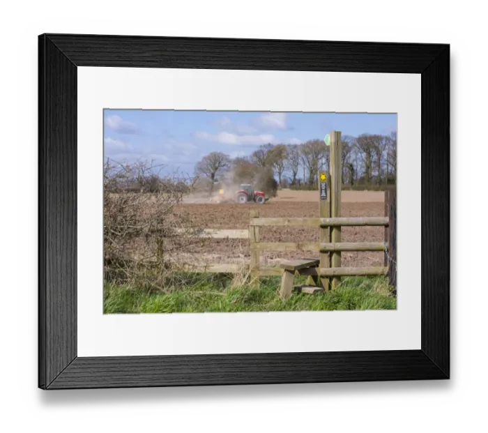 Framed Print : Public footpath sign and stile at edge of field, with Massey Ferguson tractor cultivating