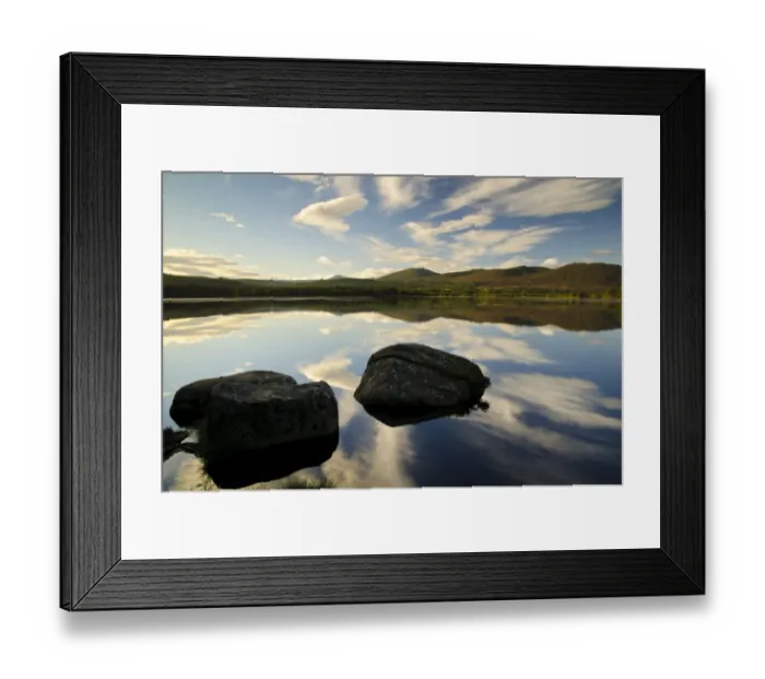 Framed Print : View of blue sky, clouds and rocks reflected in still water of freshwater loch, Loch Garten, Abernethy Forest