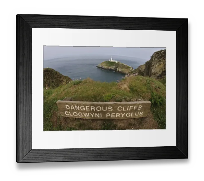 Framed Print : Dangerous Cliffs, Clogwyni Peryglus bilingual sign on clifftop, with lighthouse in background, South Stack Lighthouse Framed Print : Dangerous Cliffs, Clogwyni Peryglus bilingual sign on clifftop, with lighthouse in background, South Stack Lighthouse