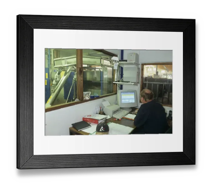 Framed Print : Dairy farming, farmer sitting at desk in office, using computer, milking machine beyond internal window, Sweden Framed Print : Dairy farming, farmer sitting at desk in office, using computer, milking machine beyond internal window, Sweden
