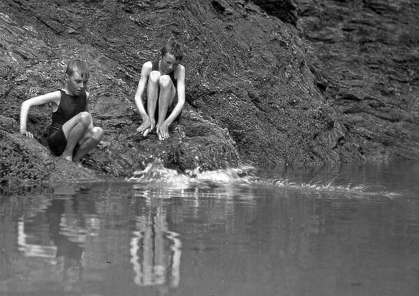 Two boys in swimsuits sitting on a rock