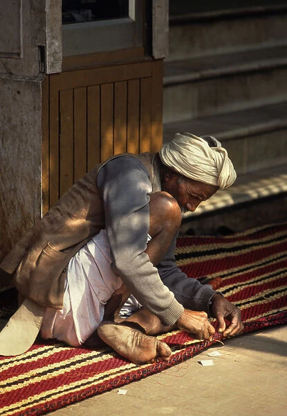 Carpet maker stitches the hem of a striped carpet, Rajasthan