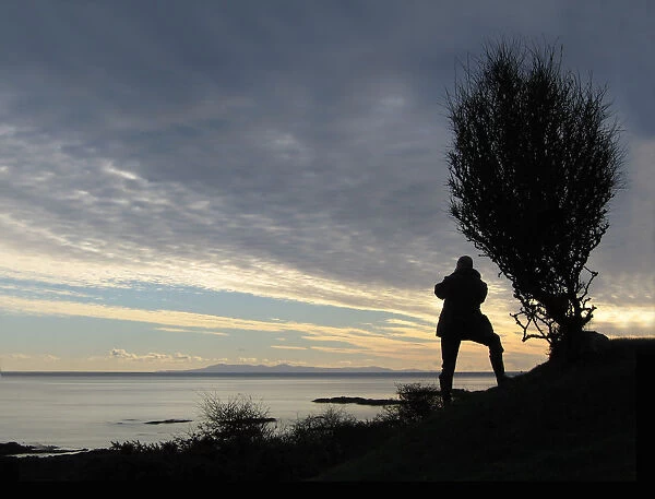 A man takes a photograph of the Isle of Man from Knockbrex