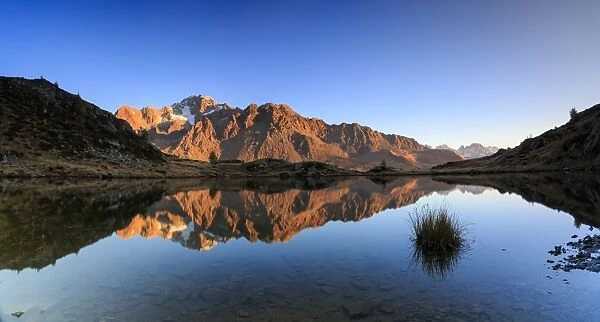 Panorama of the rocky peaks of Mount Disgrazia reflected in Lake Zana at dawn, Malenco Valley