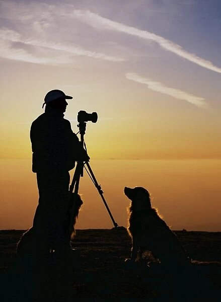 A photographer and dogs on Black Combe at sunset with the Isle of Man behind in the Lake District UK