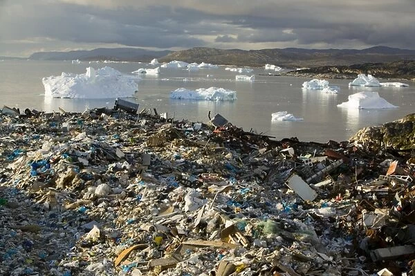 Rubbish dumped on the tundra outside Illulissat in Greenland with icebergs behind from the Sermeq Kujullaq or Illulissat Ice fjord. The Illulissat ice fjord is a Unesco world heritage