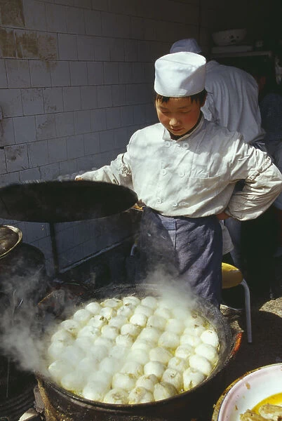 20012884. CHINA Shaanxi Province Xian Cook lifting the lid off large dish of frying food