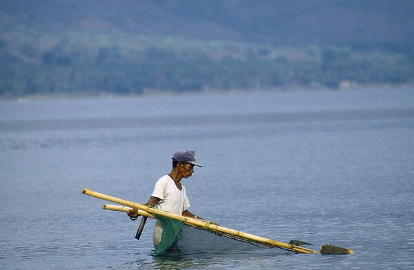 20034755. INDONESIA Palu Man fishing near beach with hand net