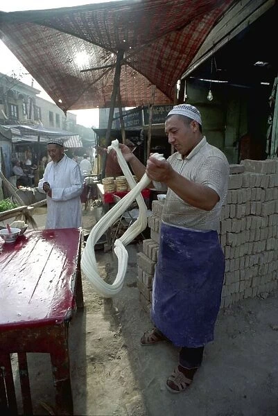 20046228. CHINA Xinjiang Kashgar Man spinning dough at a street side stall