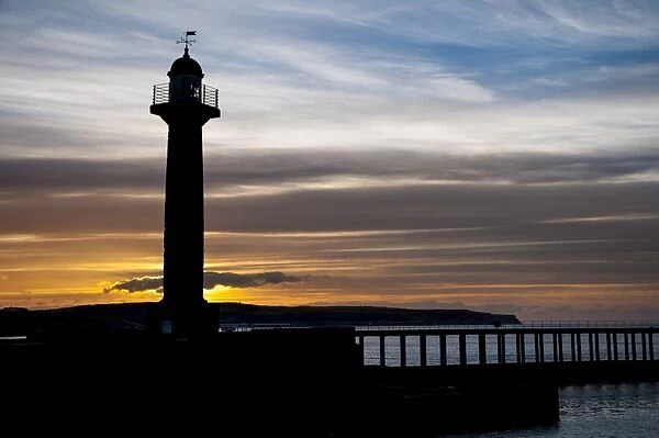 19th century stone lighthouse on pier, silhouetted at sunset, West Pier, Whitby, North Yorkshire, England, April