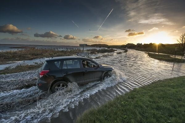 4x4 driving through flooded coast road beside coastal marshland after tidal surge, Cley Marshes Reserve