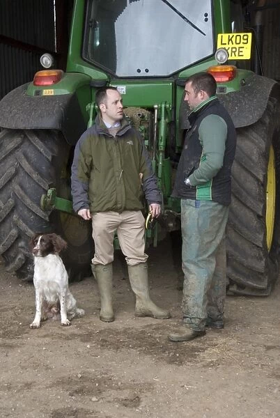 Agronomist discussing program for day with farmer, standing beside tractor, Hertfordshire, England, april
