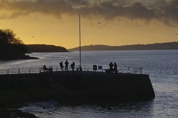 Anglers on pier silhouetted at sunset, River Kent, Arnside, Morecambe Bay, Cumbria, England, january
