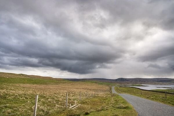Approaching stormclouds over single track road and coastline, Lunna Ness, Mainland, Shetland Islands, Scotland, June