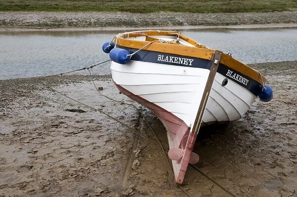 Boat moored on mud at edge of coastal creek, Blakeney, Norfolk, England, may