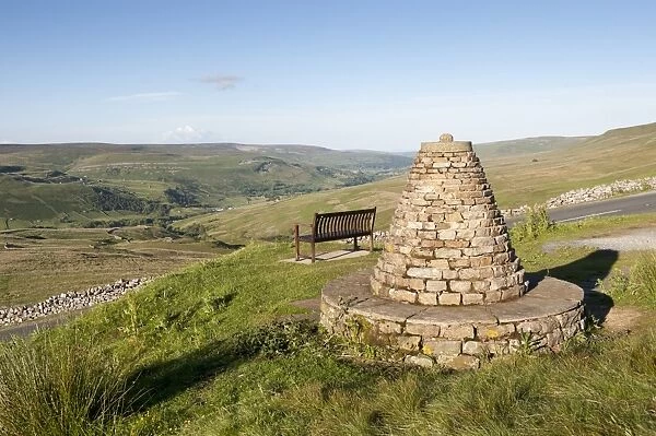 Cairn and bench on upland viewpoint overlooking valley, marking boundry of Muker Parish, Millennium Cairn