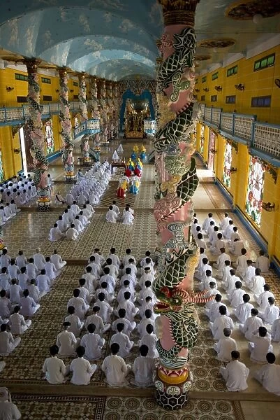 Caodaist disciples sitting beside colourful columns with dragons during ceremony, Cao Dai temple, Tay Ninh Holy See