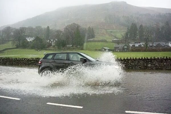 Car driving through floodwater on road during heavy rainfall, A591, Grasmere, Lake District, Cumbria, England, December