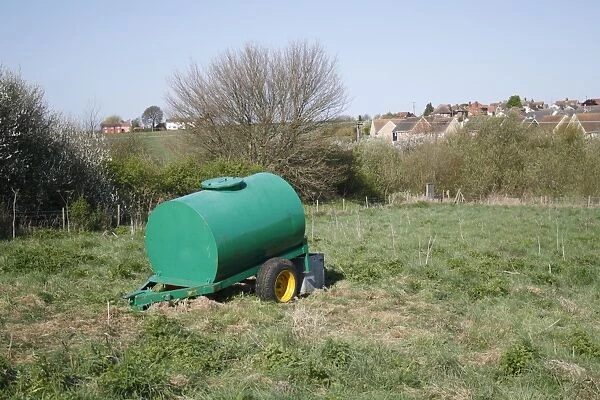 Cattle farming, water bowser in pasture, with village in background, Church Meadow Local Nature Reserve, Combs Ford