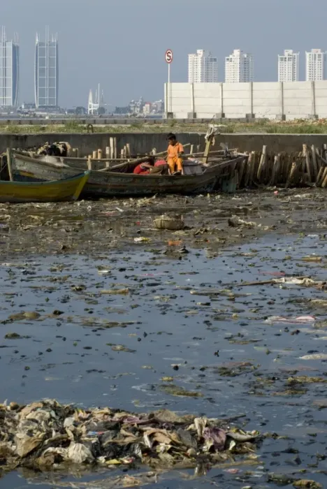 Framed Print : Children on boat in rubbish filled water, with city skyscrapers in background, Muara Karang, Jakarta, Java, Indonesia Framed Print : Children on boat in rubbish filled water, with city skyscrapers in background, Muara Karang, Jakarta, Java, Indonesia