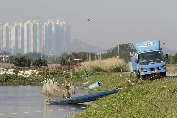 Commercial fishpond with sacks of fish food (bread crusts), boat, net and lorry, with skyscrapers in background