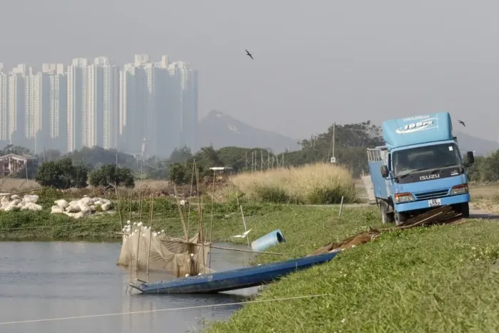 Framed Print : Commercial fishpond with sacks of fish food (bread crusts), boat, net and lorry, with skyscrapers in background