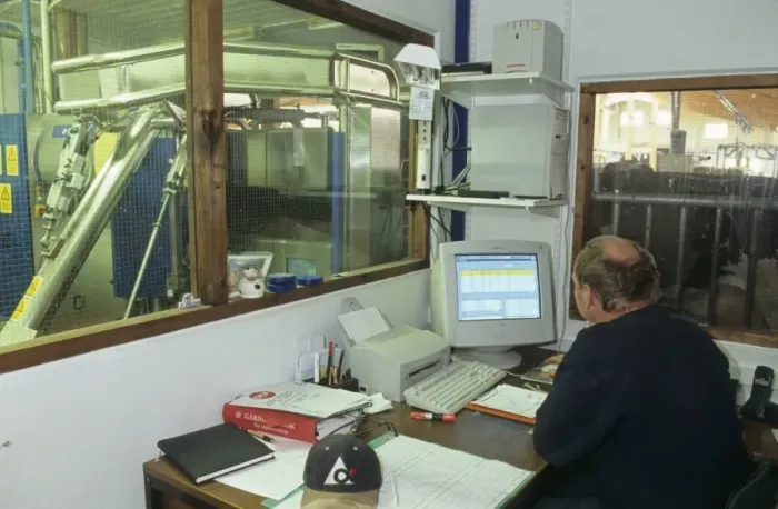 Framed Print : Dairy farming, farmer sitting at desk in office, using computer, milking machine beyond internal window, Sweden Framed Print : Dairy farming, farmer sitting at desk in office, using computer, milking machine beyond internal window, Sweden