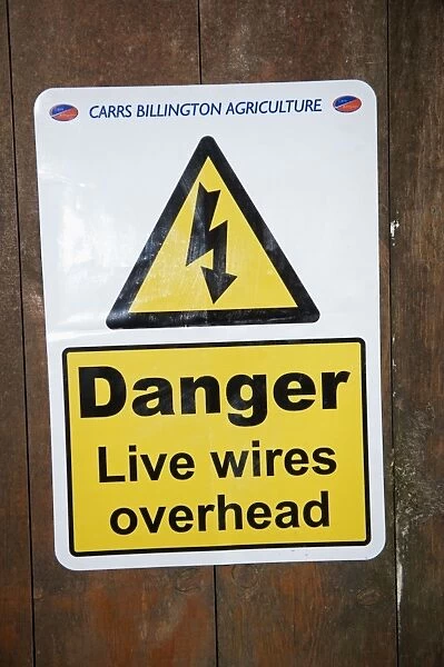 Danger, Live wires overhead sign warning of low power cables on door of farm feed store, England, April