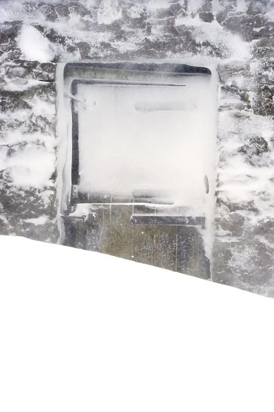 Doors on stone field barn behind snowdrift during snowstorm, Cumbria, England, March