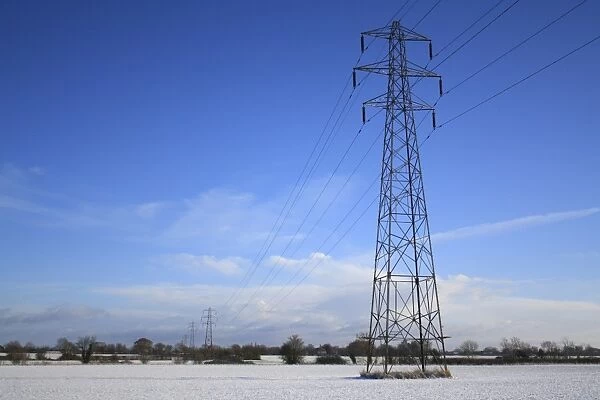 Electricity transmission pylons and overhead wires, crossing over snow covered arable farmland, Bacton, Suffolk, England, november