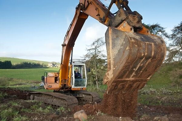 Excavator digging stone on hillside, England, november