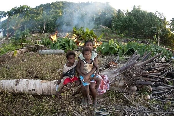 Family sitting on fallen tree near burning rubbish, Warmindi, Birds Head Peninsula, Raja Ampat Islands (Four Kings)