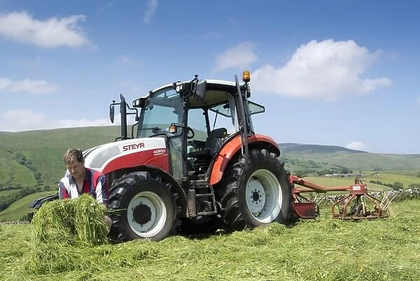 Farmer checking quality of mown grass, beside Steyr tractor with tedder, Cumbria, England, July