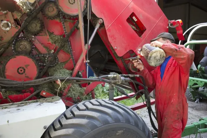 Framed Print : Farmer greasing chain on round baler, Sweden, july