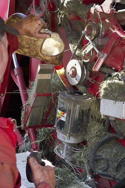 Farmer pouring grease into round baler, Sweden, july