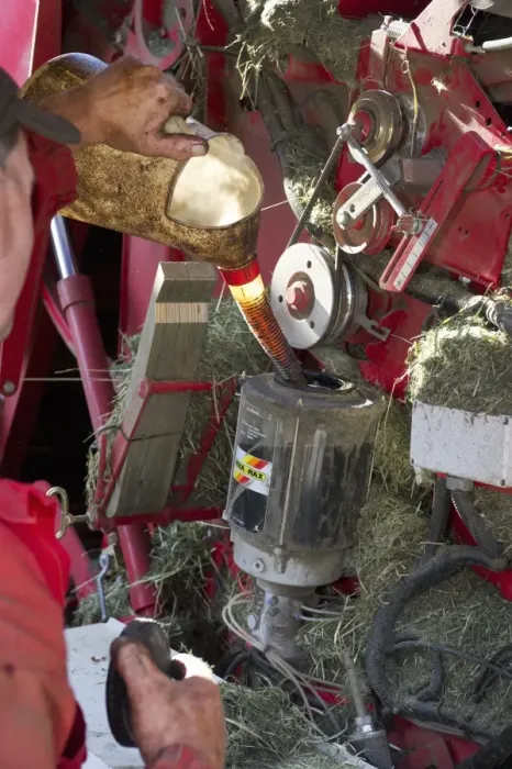 Framed Print : Farmer pouring grease into round baler, Sweden, july