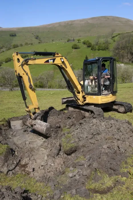 Framed Print : Farmer repairing old blocked drain in upland meadow using mini digger, Cumbria, England, May