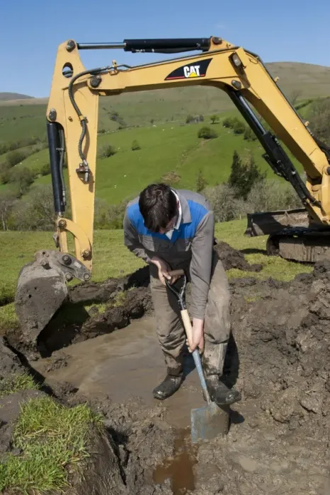 Framed Print : Farmer repairing old blocked drain in upland meadow using mini digger and spade, Cumbria, England, May Framed Print : Farmer repairing old blocked drain in upland meadow using mini digger and spade, Cumbria, England, May