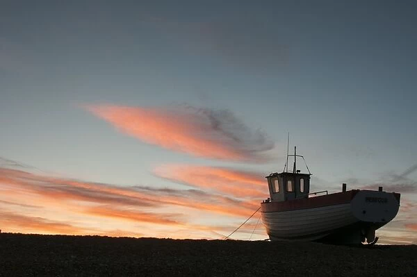 Fishing boat hauled up on shingle beach at sunset, Dungeness, Kent, England, September