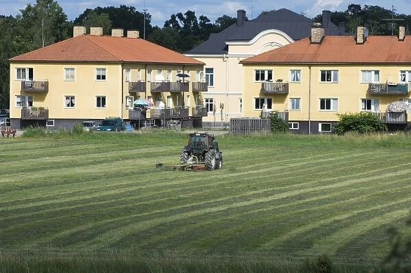 Hay crop, tractor tedding hay, field next to houses, Sweden