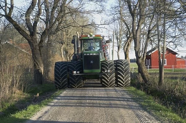 John Deere 9400 tractor, with dual wheels, driving along small road on way to fields, Uppland, Sweden, may