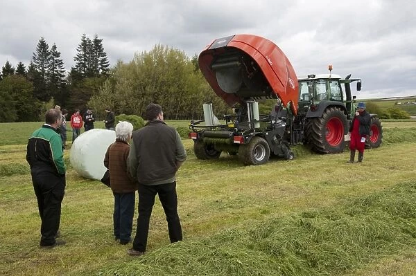 Kuhn all in one baler and wrapper, wrapping round silage bale in plastic at demonstration with farmers watching