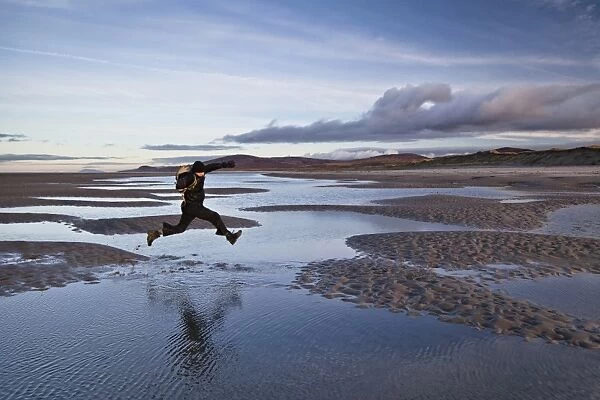 Man jumping over tidal sea puddles, Killinalan Point, Loch Gruinart, Isle of Islay, Inner Hebrides, Scotland