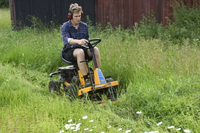 Framed Print : Man using ride-on mower on farm, cutting long grass around sheds, Sweden Framed Print : Man using ride-on mower on farm, cutting long grass around sheds, Sweden