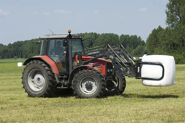 Massey Ferguson 6290 tractor with mechanical loader, carrying plastic wrapped round silage bale, Sweden